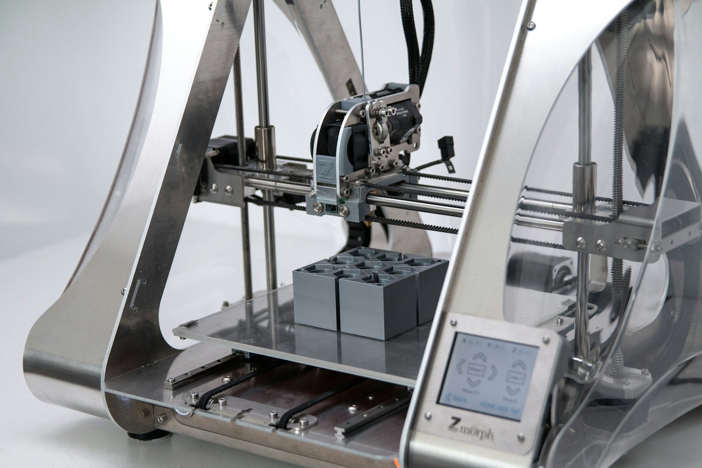 Ein 3D-Drucker erstellt graue Objekte auf seiner Plattform.